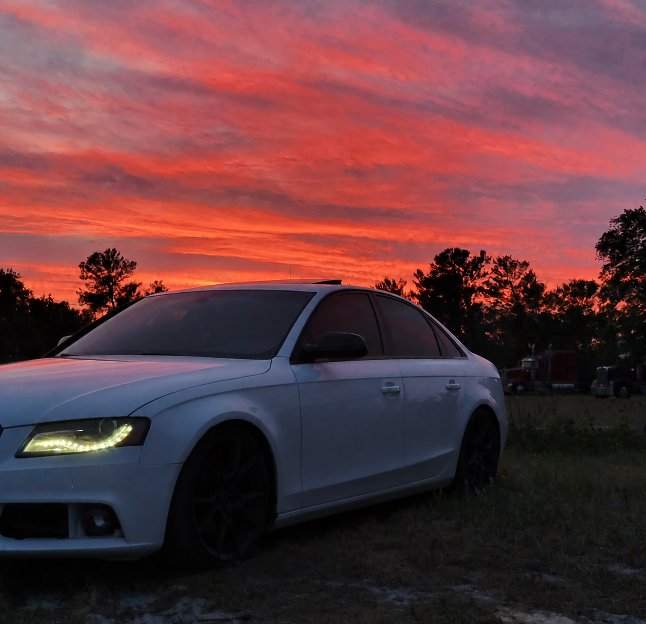 Polaks_Garage white sedan beneath a vivid orange and pink sunset